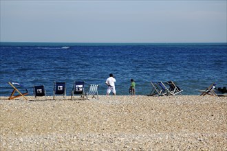 ENGLAND, East Sussex, Eastbourne, Man and young boy on the beach with deck chairs blowing in the
