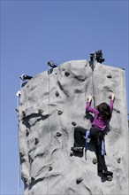 USA, Georgia, Savannah, Young girl climbing manmade rockface using safety harness.