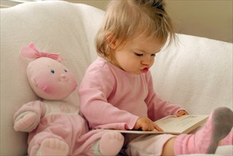 EDUCATION, Children, Reading, Infant girl dressed in pink reading book whilst mouthing the words