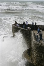 ENGLAND, East Sussex, Brighton, "Seafront, Tourists With waves crashing against sea defences."