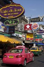 THAILAND, Central, Bangkok, Khaosan Road. Pink Taxi parked beneath colourful advertising signs.