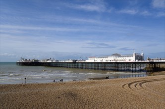 ENGLAND, East Sussex, Brighton, The Pier at low tide with people on the shingle pebble beach.