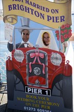 ENGLAND, East Sussex, Brighton, Man and woman with their faces in amusement cut-out of wedding car