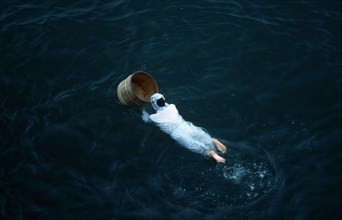 Japan, Honshu, Toba, Traditional female pearl diver swimming in the water with wooden barrel for