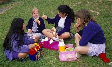 England, East Sussex, Brighton, Four young schoolgirls sitting on the grass in the school playing