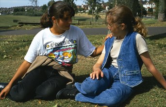 England, East Sussex, Brighton, One teenage girl reassuring another young girl sitting on the grass