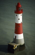 England, East Sussex, Beachy Head, The red and white hooped lighthouse in the sea off the coast.