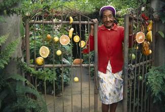 CUBA, Pinar del Rio, Vinales, Elderly woman smiling at gateway to garden hung with pieces of fruit.