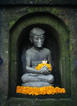 Indonesia, Bali, Ubud, Stone statue of male figure in niche of wall sitting in lotus position