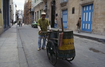 CUBA, Havana, Street cleaner pushing hand cart and smoking cigar.