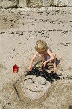 England, East Sussex, Brighton, Young boy making a sand sculpture of a face in the sand on the