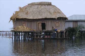 Benin, Ganvie, Thatched house on stilts in West African lake town, woman and children on a boat