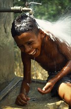 Dominican Republic, Laughing boy with head under water tap.