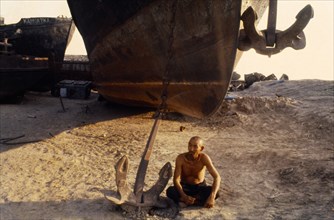 Uzbekistan, Near Aral Sea, Indigenous old man sitting beside a beached boat and anchor