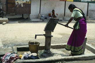 India, Andhra, Pradesh, Pochampally, Young woman drawing water at hand pump in street.