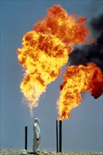 Saudi Arabia, Arab man standing next to gas burning off from oil well.