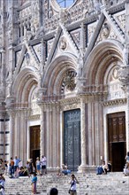 ITALY, Tuscany, Siena, Tourists on the steps of the pink black and white marble facade of the 13th