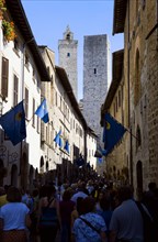 ITALY, Tuscany, San Gimignano, Via di Querececchio lined with flags and busy with tourists walking