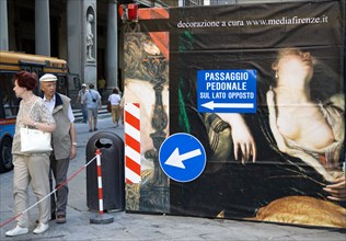 ITALY, Tuscany, Florence, Tourist couple walking past a billboard outside the Uffizi Gallery that