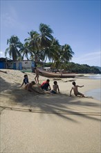 VENEZUELA, Margarita Island, Playa la Galera,  Kids playing on the beach, under the shade of a palm