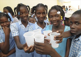 HAITI, Isla de la Laganave, School children holding plastic cups of water from plumbing paid for by