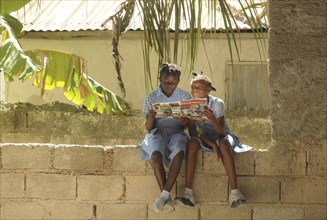 HAITI, Isla de la Laganave, young school girls sat on wall reading geography magazine.