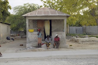 Haiti, Isla de Laganave, local people sat outside hime with tin roof.