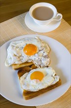 Food, Cooked, Meals, A breakfast table setting of two fried eggs on toast on a plate beside a cup