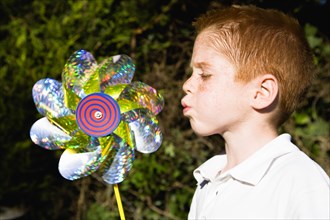 Children, Toys, Outdoors, Young red haired boy blowing toy windmill gently.
