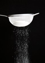 Food, Cooking, Baking, White plain flour being siifted through a sieve against a black background.