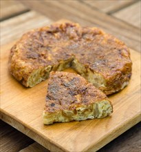 Food, Cooked, Eggs, Spanish omelette or tortilla on a wooden chopping board with a slice cut out.