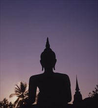 Thailand, Sukhothai, Wat Mahathat, Seated Buddha Statue silhouetted against purple coloured evening