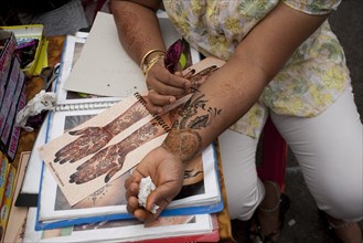 Singapore, Little India, Thieves MArket, Woman painting Henna Tattoo on her own arm whilst leaning