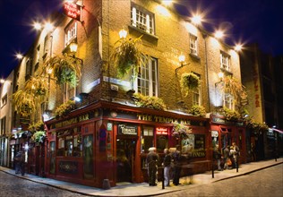 Ireland, County Dublin, Dublin City, Temple Bar Pub illuminated at night with people walking past