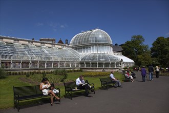 Ireland, Northern, Belfast, Botanic Gardens with people sat on benches outside the Palm House next