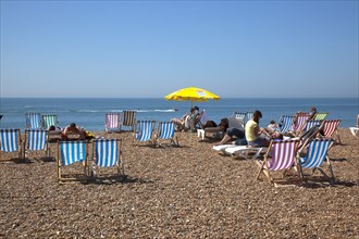 England, East Sussex, Brighton, Deck chairs and sunbathers on the pebble beach.