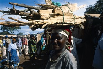 Great Lakes Region, West, Tanzania. Refugee woman carrying bundle of firewood on her head. Refugees