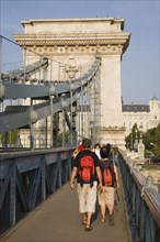 Budapest, Pest County, Hungary. Tourists with matching day packs crossing Szechenyi Chain Bridge or