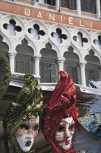 Venice, Veneto, Italy. Red green blue and gold carnival masks in front of partly seen facade of the