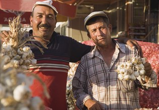 Kusadasi, Aydin Province, Turkey. Stallholders at weekly market with sacks of garlic for sale and