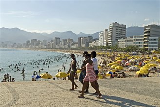 Rio de Janeiro, Brazil. Crowds at Ipanema beach with yellow umbrellas blue sea and sky swimmers in