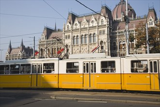 Budapest, Pest County, Hungary. Yellow tram passing the Parliament Building. Hungary Hungarian
