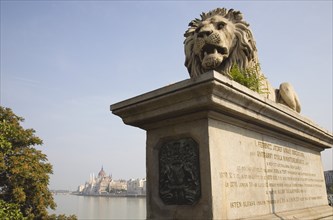Budapest, Pest County, Hungary. Lion sculpture on the Chain Bridge with Hungarian Parliament