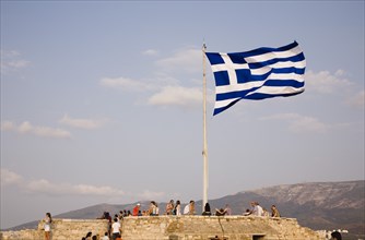 Athens, Attica, Greece. Acropolis Greek flag flying with tourists admiring view of the city. Greece
