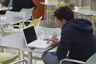 Vienna, Austria. Neubau District. Young man having coffee while surfing the net on laptop at the