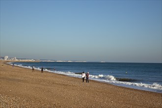 Shoreham-by-Sea, West Sussex, England. People walking along the waters edge on Shoreham beach.