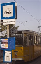 Budapest, Pest County, Hungary. Yellow tram approaching stop and signpost displaying timetable.