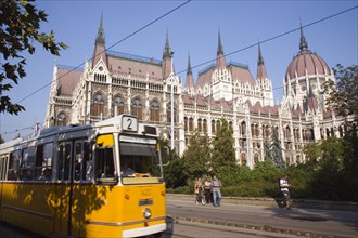 Budapest, Pest County, Hungary. Yellow tram passing the Neo-Gothic exterior facade of the