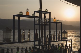 Samos, Northern Aegean, Greece. Vathy. Sun setting over water behind open air bar with the Ampelos