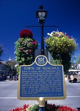 Niagara on the Lake, Ontario, Canada. Queen Street. Plaque and hanging baskets. Blue Canadian